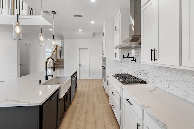 kitchen featuring light stone countertops, white cabinetry, wall chimney exhaust hood, hanging light fixtures, and stainless steel gas cooktop