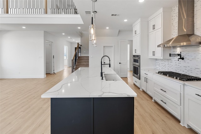 kitchen featuring a spacious island, wall chimney range hood, and appliances with stainless steel finishes