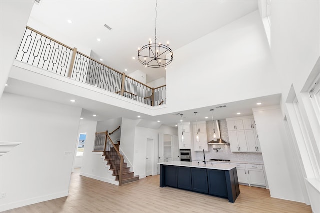 kitchen with a kitchen island with sink, a high ceiling, white cabinets, hanging light fixtures, and wall chimney exhaust hood