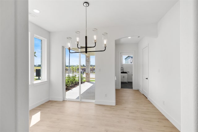 unfurnished dining area with light hardwood / wood-style flooring, a chandelier, and sink