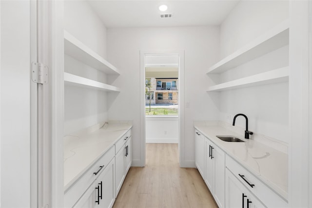 bar featuring light stone counters, sink, and white cabinets