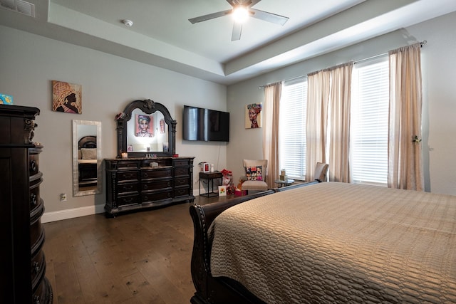 bedroom with dark wood-style flooring, a ceiling fan, visible vents, baseboards, and a raised ceiling