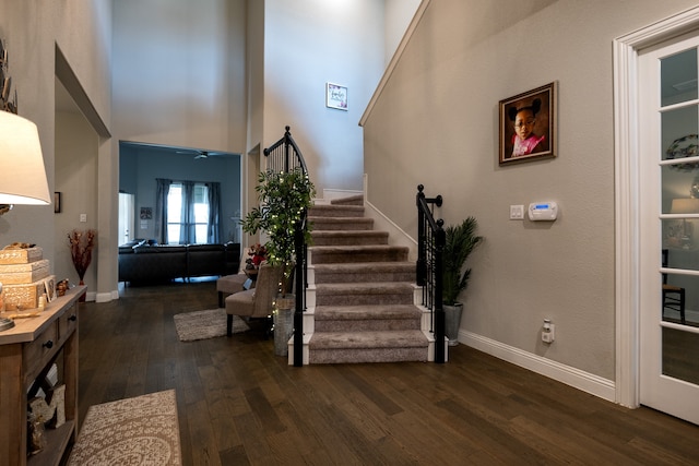 foyer entrance featuring a towering ceiling, dark wood-style floors, baseboards, and stairway