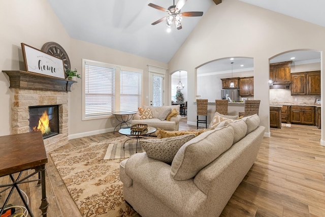 living room with a fireplace, ceiling fan, ornamental molding, light wood-type flooring, and high vaulted ceiling