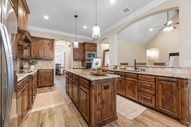 kitchen with light stone countertops, tasteful backsplash, a kitchen island, sink, and appliances with stainless steel finishes