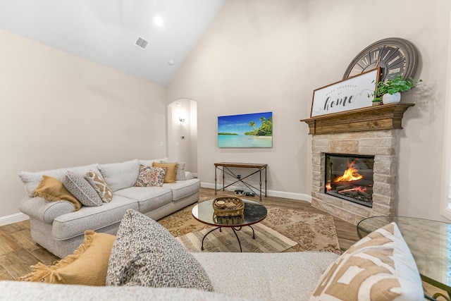 living room featuring a stone fireplace, high vaulted ceiling, and wood-type flooring