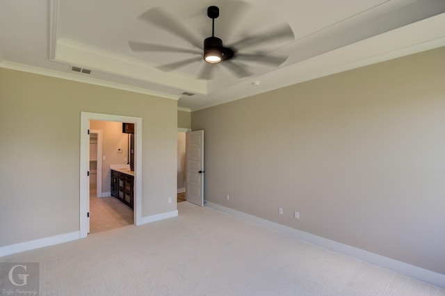 unfurnished bedroom with ensuite bathroom, ceiling fan, a tray ceiling, light colored carpet, and crown molding