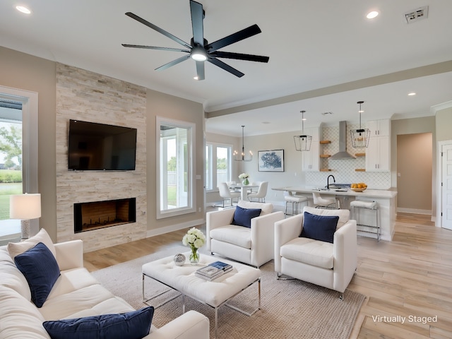 living room featuring ceiling fan, light wood-type flooring, a fireplace, and sink