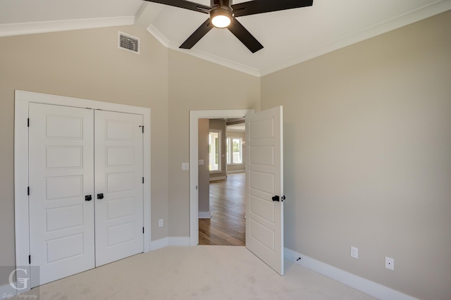 unfurnished bedroom with ceiling fan, a closet, light colored carpet, vaulted ceiling with beams, and ornamental molding