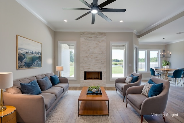 living room with light hardwood / wood-style floors, ceiling fan with notable chandelier, ornamental molding, and a fireplace