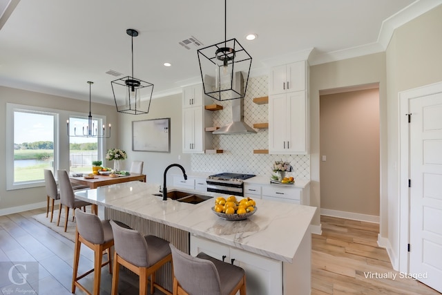 kitchen featuring stainless steel gas range, white cabinetry, an island with sink, decorative backsplash, and sink