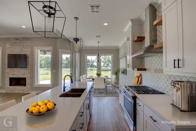 kitchen with sink, white cabinetry, wall chimney exhaust hood, and stainless steel gas range oven