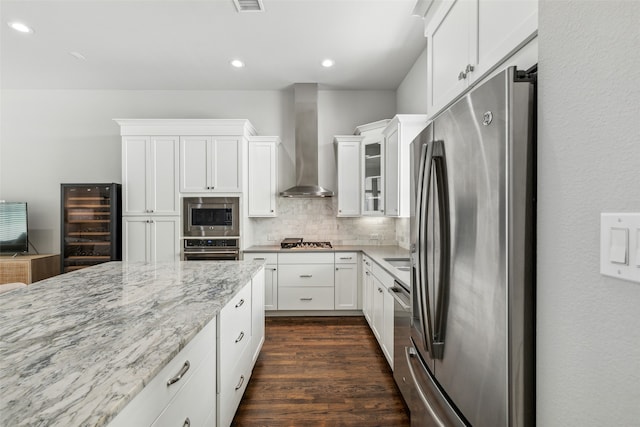 kitchen with wall chimney range hood, dark hardwood / wood-style flooring, stainless steel appliances, tasteful backsplash, and white cabinetry