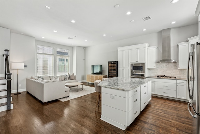 kitchen with wall chimney range hood, a kitchen island, dark wood-type flooring, white cabinets, and appliances with stainless steel finishes