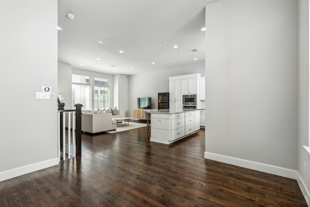 kitchen featuring light stone countertops, stainless steel microwave, dark hardwood / wood-style flooring, a center island, and white cabinets