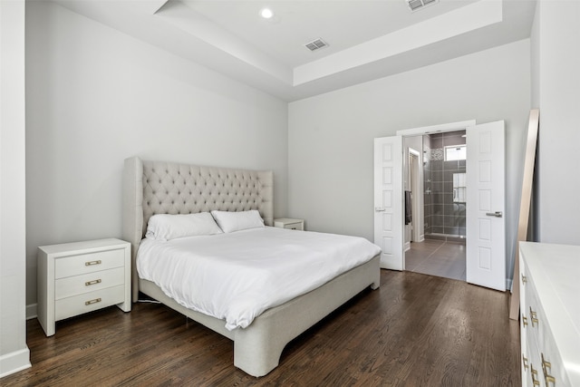 bedroom with dark tile floors, a raised ceiling, and ensuite bath