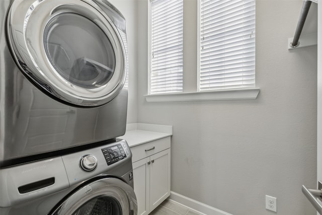 laundry room featuring stacked washing maching and dryer, cabinets, and light tile floors