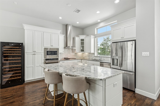 kitchen featuring a center island, wall chimney range hood, appliances with stainless steel finishes, beverage cooler, and tasteful backsplash