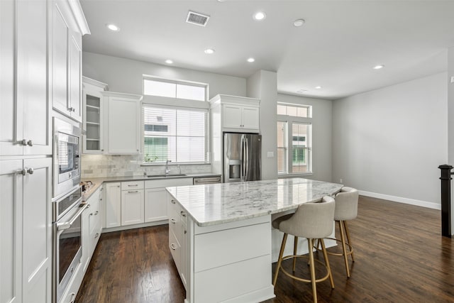 kitchen with dark wood-type flooring, backsplash, a kitchen island, white cabinetry, and appliances with stainless steel finishes