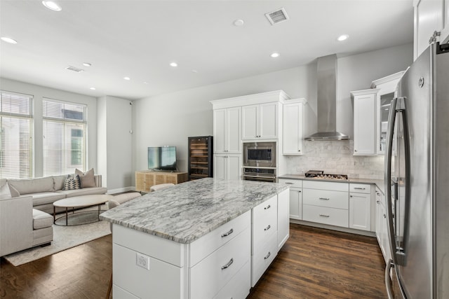 kitchen featuring tasteful backsplash, dark hardwood / wood-style flooring, a kitchen island, wall chimney range hood, and appliances with stainless steel finishes