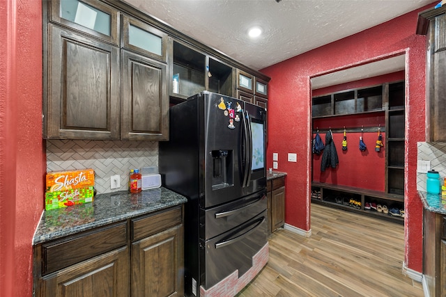 kitchen featuring black fridge, light hardwood / wood-style floors, a textured ceiling, dark stone counters, and backsplash