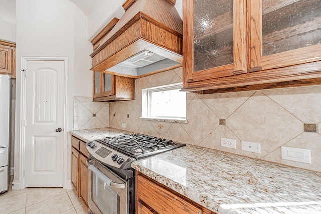 kitchen with light stone counters, light tile flooring, stainless steel appliances, tasteful backsplash, and premium range hood