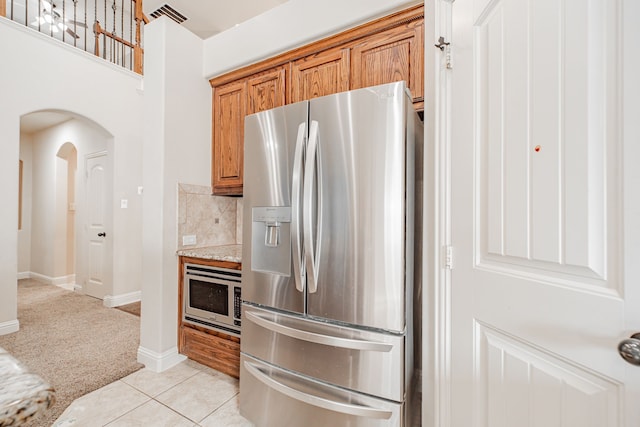 kitchen featuring stainless steel appliances, light stone countertops, light tile flooring, and tasteful backsplash