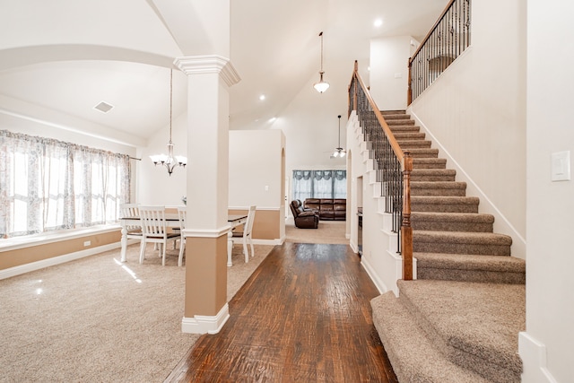 foyer entrance featuring high vaulted ceiling, carpet flooring, ornate columns, and a notable chandelier