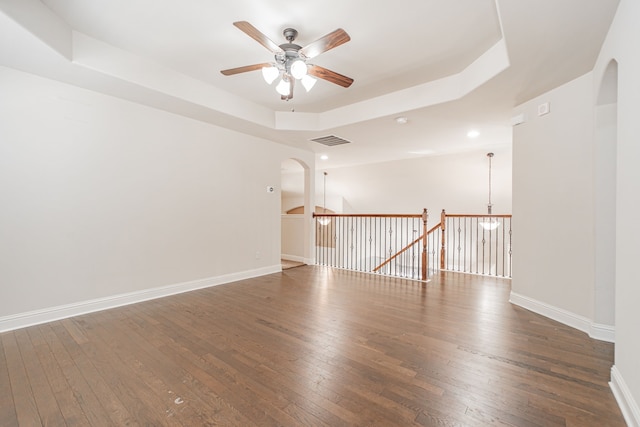 empty room with a tray ceiling, dark wood-type flooring, and ceiling fan