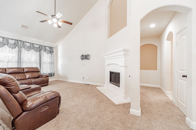 living room with high vaulted ceiling, ceiling fan, a high end fireplace, and light colored carpet