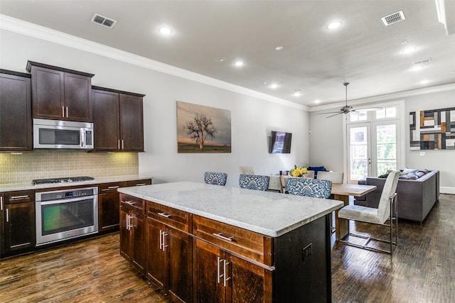 kitchen with dark hardwood / wood-style flooring, backsplash, ceiling fan, a center island, and appliances with stainless steel finishes