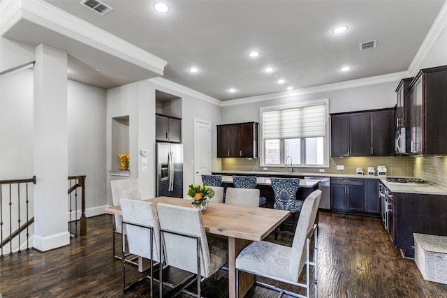 kitchen with dark wood-type flooring, appliances with stainless steel finishes, tasteful backsplash, and crown molding