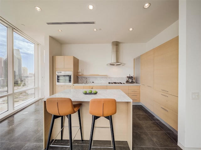 kitchen with a center island, floor to ceiling windows, white oven, wall chimney exhaust hood, and light brown cabinetry