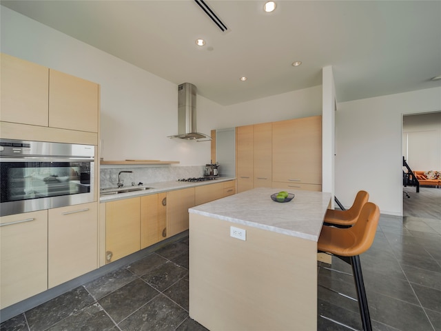 kitchen with sink, wall chimney exhaust hood, stainless steel appliances, light brown cabinets, and a kitchen island