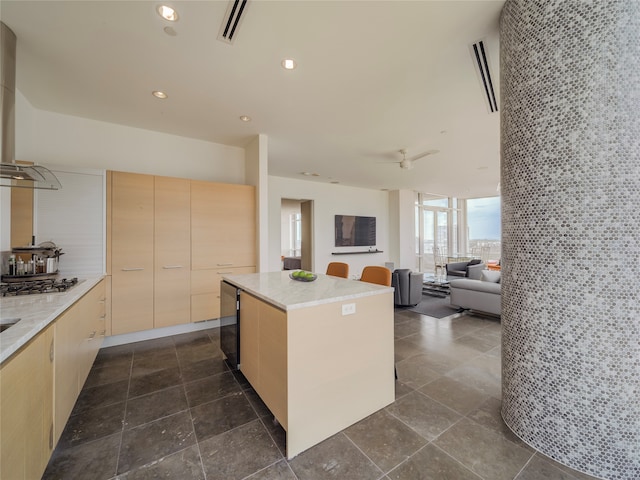 kitchen featuring a center island, ceiling fan, light brown cabinetry, a wall of windows, and stainless steel gas cooktop