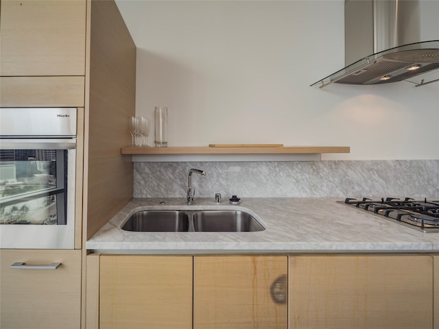 kitchen with oven, wall chimney range hood, sink, gas stovetop, and light brown cabinetry