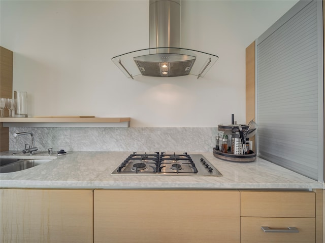 kitchen with stainless steel gas stovetop, light brown cabinets, sink, island range hood, and light stone counters