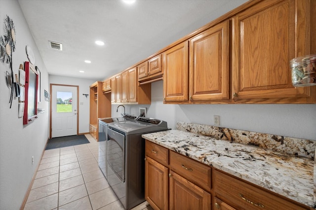 clothes washing area with washing machine and clothes dryer, light tile patterned floors, and cabinets