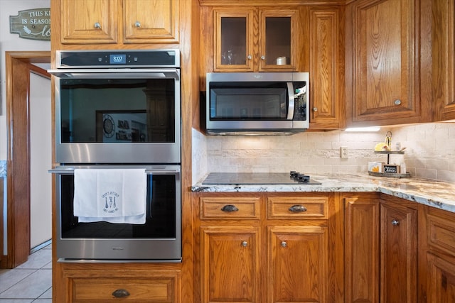 kitchen with light tile patterned flooring, light stone counters, stainless steel appliances, and tasteful backsplash