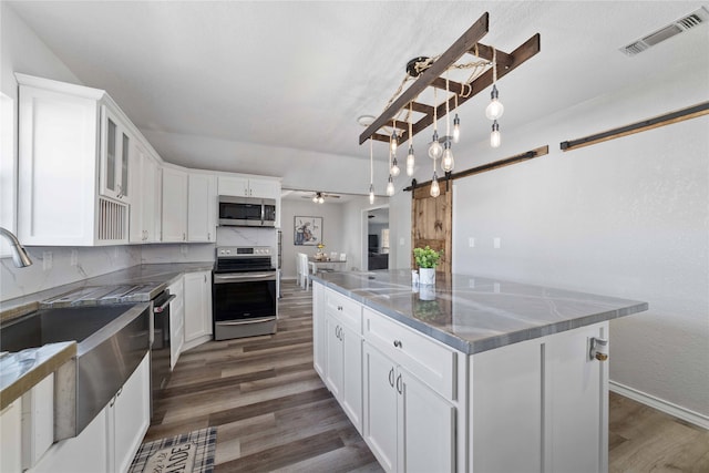 kitchen with appliances with stainless steel finishes, white cabinets, dark hardwood / wood-style floors, and a kitchen island