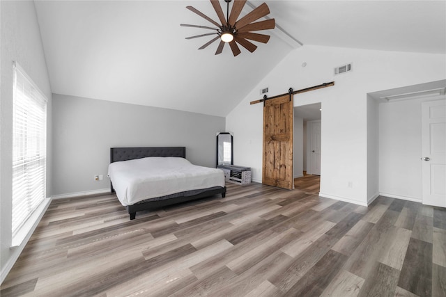 unfurnished bedroom with a barn door, high vaulted ceiling, hardwood / wood-style flooring, and ceiling fan