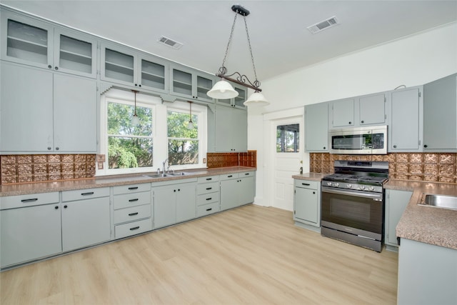 kitchen with appliances with stainless steel finishes, backsplash, sink, decorative light fixtures, and light hardwood / wood-style floors