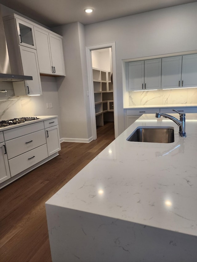 kitchen featuring white cabinets, light stone countertops, sink, and wall chimney range hood