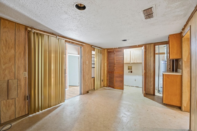 unfurnished room featuring water heater, a textured ceiling, and wood walls