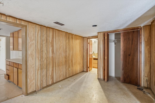 unfurnished bedroom featuring wood walls, connected bathroom, and a textured ceiling