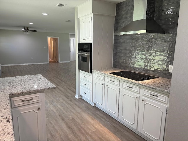 kitchen with wall chimney range hood, light hardwood / wood-style flooring, black electric stovetop, oven, and tasteful backsplash