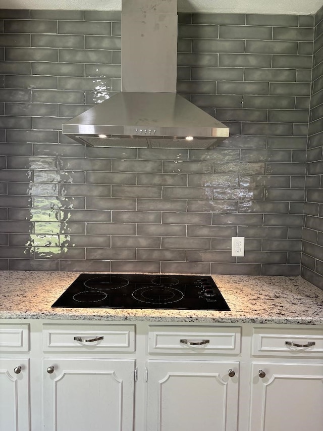 kitchen with wall chimney exhaust hood, black electric stovetop, tasteful backsplash, and white cabinetry