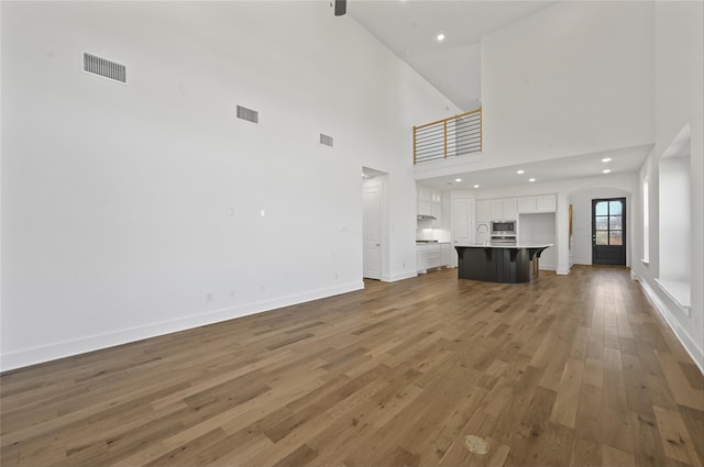 unfurnished living room with light wood-type flooring and high vaulted ceiling