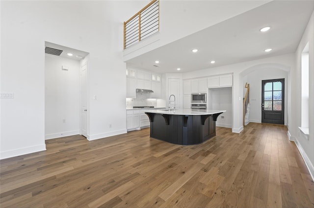 kitchen with wood-type flooring, an island with sink, a kitchen bar, stainless steel appliances, and white cabinets