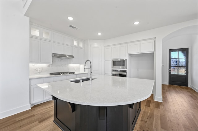 kitchen with a kitchen island with sink, stainless steel appliances, sink, white cabinets, and light hardwood / wood-style floors